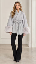 Front view of model wearing grey wrap coat with faux fur cuffs and black flared pants