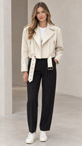 Front view of woman wearing cream cropped faux leather moto jacket with belt and black trousers