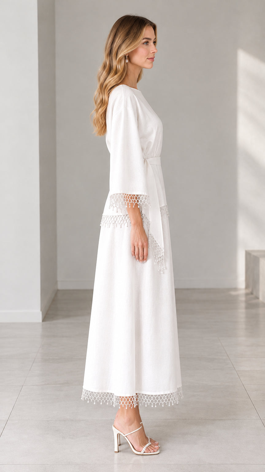Side profile view of woman modeling white elegant crochet trimmed maxi dress